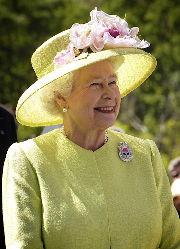 Queen Elizabeth in a yellow hat and dress posing for a photo. 