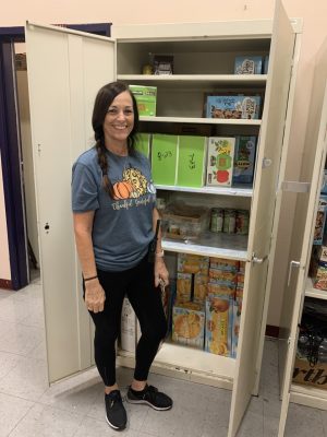Ms. Kaylene Barker stands in front of a food storage closet proudly showing the donated food for the families in need.