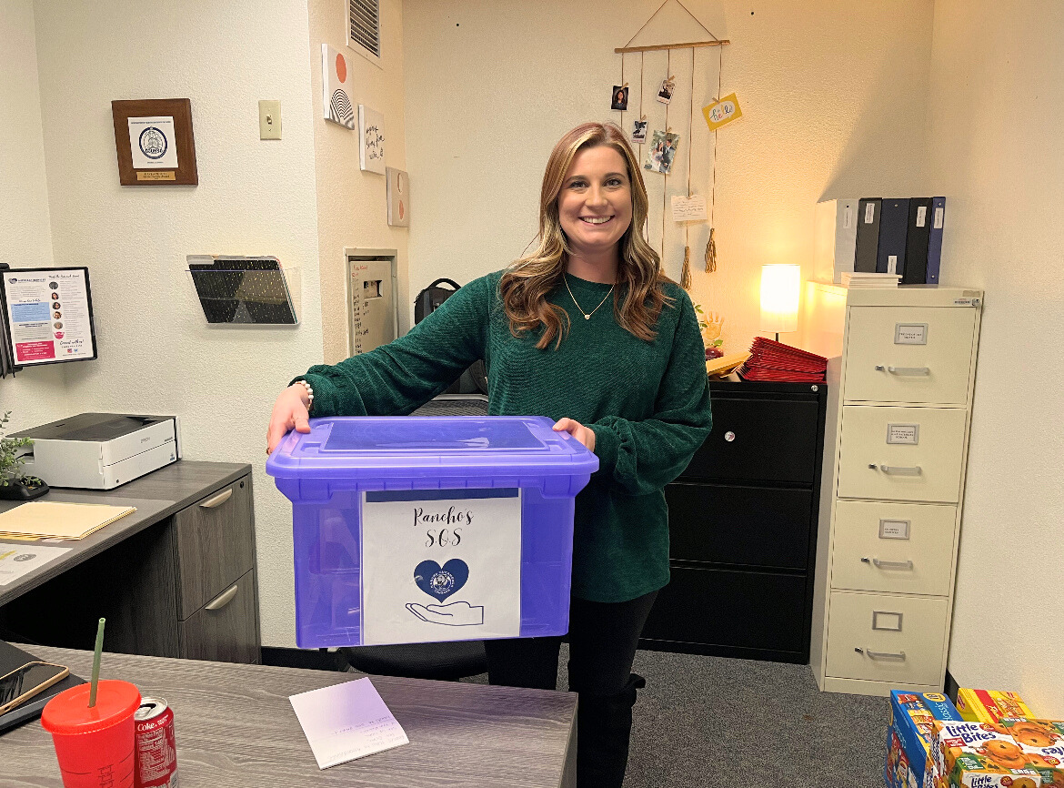 Photo caption: Ms. Kayla Peters stands proudly with the S.O.S. donation box in her office.