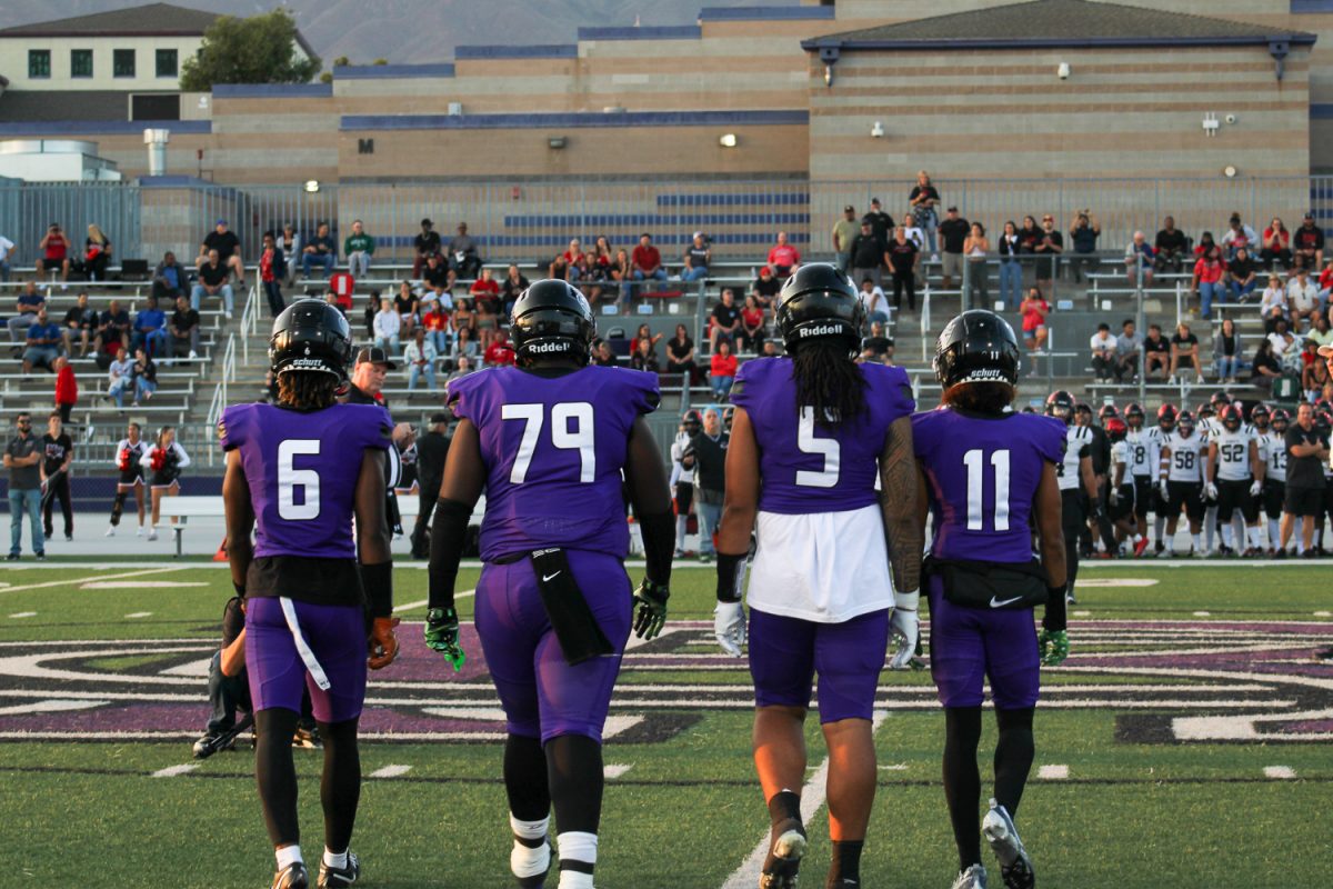 Four Varsity football players walk onto the field to prepare for the coin toss at the start of the game.