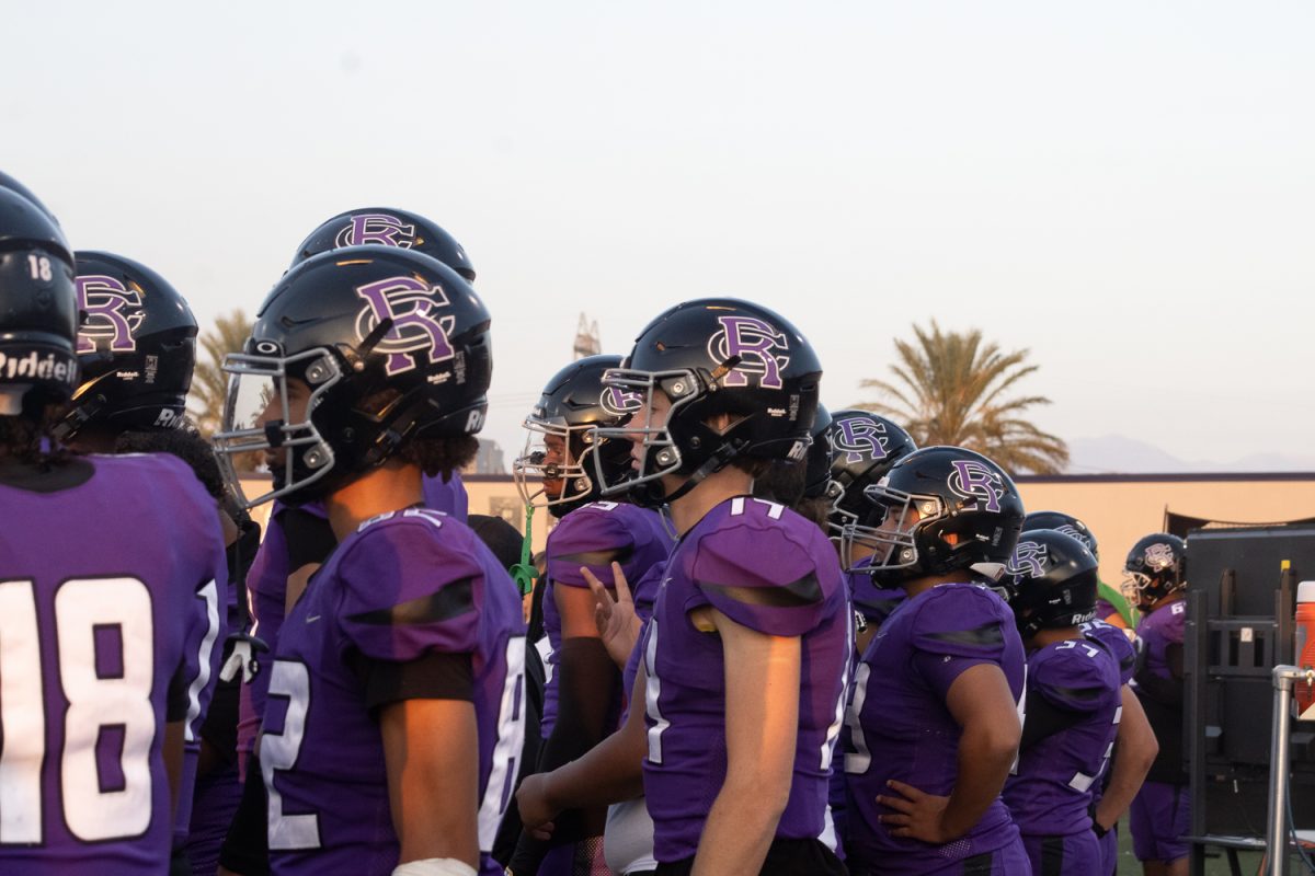 RCHS Varsity football players watch from the sideline as their teammates fight for a touchdown.