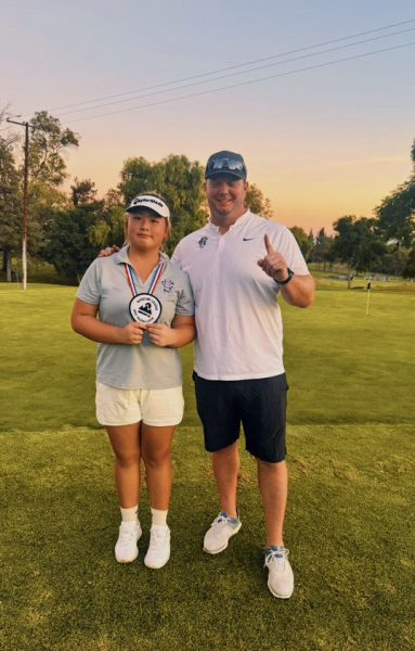 Junior Emily Zhang poses with head golf coach Mr. Dale Rogers while holding her Baseline League patch.