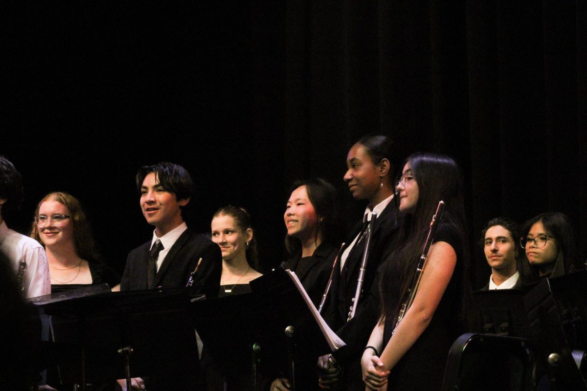 Concluding their section of the concert, members of the symphonic band stand and smile as the audience applauds their performance.