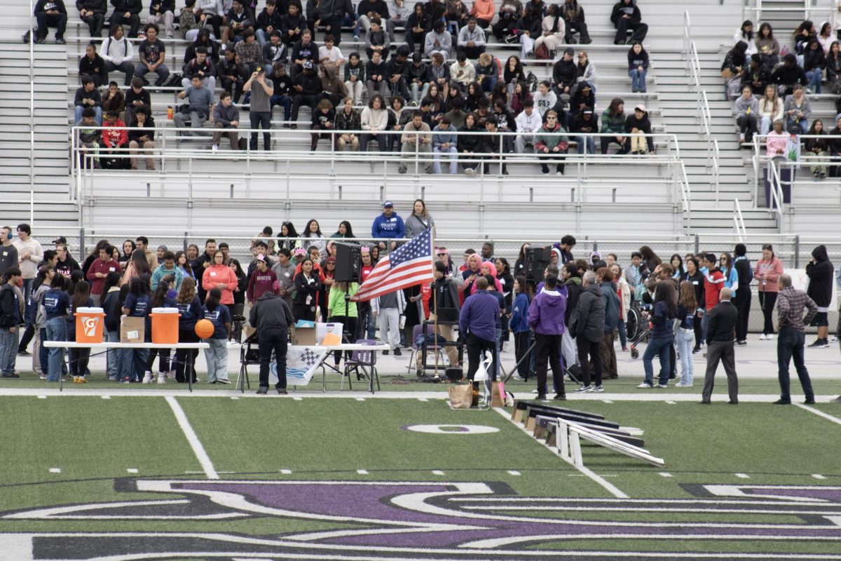 People stand during the singing of the national anthem before the start of the Cougar Relays. 