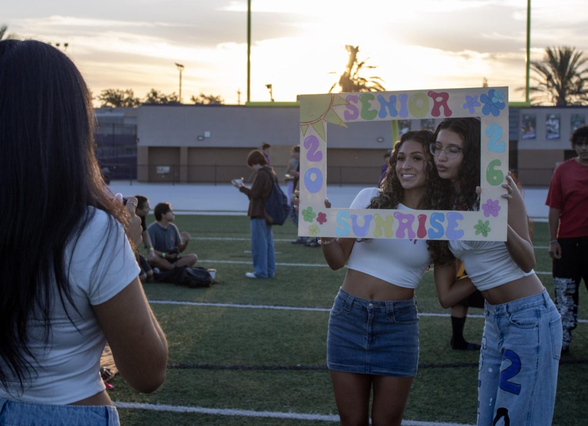 On Cougar Stadium's field, two seniors pose with a sign in front of the sunrise as their friend gets ready to snap a picture.