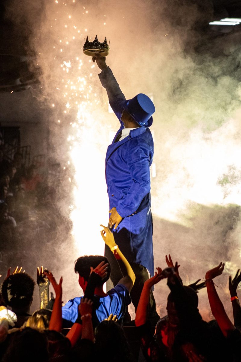 The 2025 homecoming rally comes to an end with RCHS principal Mr.Azande Aikens standing on the center platform holding up a crown. As he holds up the crown, pyrotechnics erupt around him, and students flood the gym floor around him.