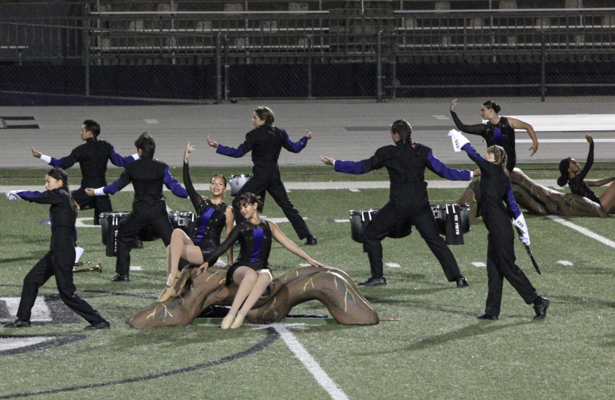 Seniors Khloe Gonzalez and Emma Perea sit together on a part of the tree prop while other performers surround them.