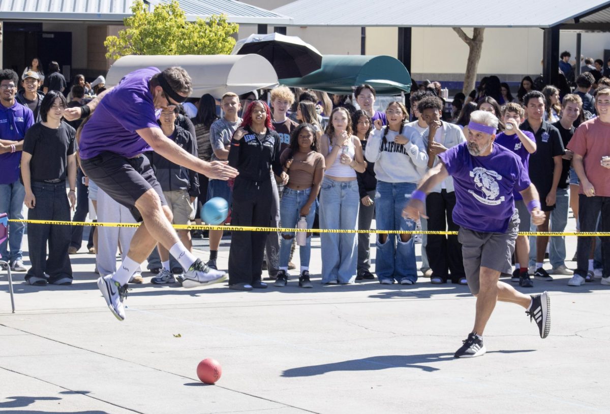 The physical education teacher jumps up to dodge a ball thrown by the blank teacher Mr. (blank) (blank during the annual staff dodge ball game.