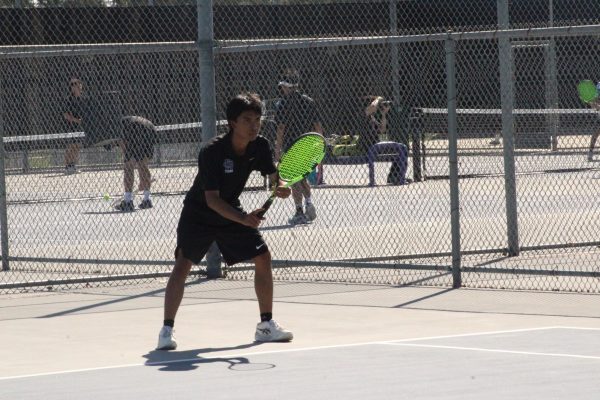 Varsity tennis player Jarett Soriano gets ready to receive a serve from the opposing team.