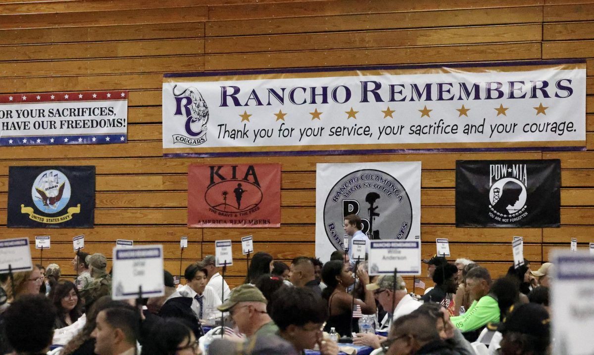 A display of the Rancho Remembers sign hangs above the veterans and students. 
